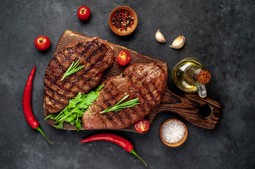 Obraz na płótnie Canvas Tasty two grilled beef steaks with spices and herbs on a cutting board on a stone background