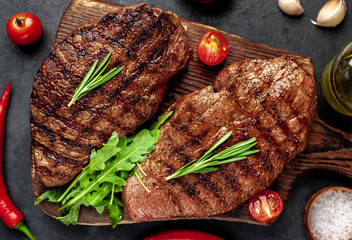 Tasty two grilled beef steaks with spices and herbs on a cutting board on a stone background