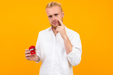 blond European man makes a proposal holding a ring in a red box on a yellow background.