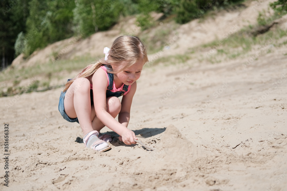 Wall mural little girl playing with a sand and building sandcastle. cute little girl spending time on sea coast