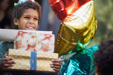 Kids birthday party . Little boy in birthday cap holding pile of birthday presents.