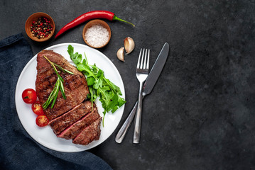 Grilled beef steak with spices, tomatoes and herbs on a white plate on a stone background with copy space for your text.