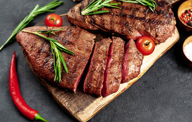 Tasty two grilled beef steaks with spices and herbs on a cutting board on a stone background