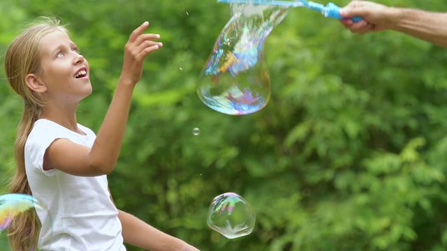 Girl playing with soap bubbles outdoor.  Nine-year-old girl plays with soap bubbles in the summer garden. Slow motion.