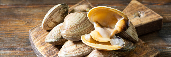 Raw clams on a wooden Board on a brown wooden table. Rustic banner