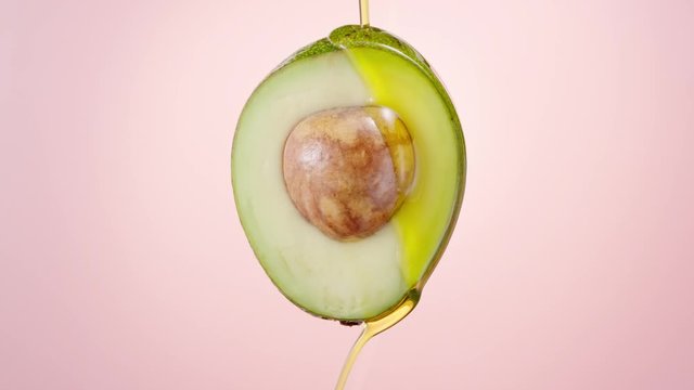 Fresh cut avocado covered with oil on nude pink background. Avocado oil pouring. Fresh cut avocado with oil stream. Slow motion, 4K 