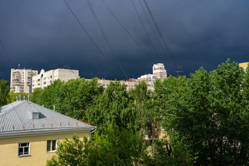 Town landscape before the storm with sunlit buildings and green trees and dark gloomy sky