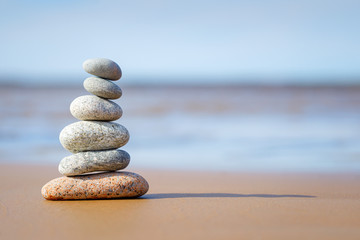 Pyramid stones balance on the sand of the beach. The object is in focus, the background is blurred.