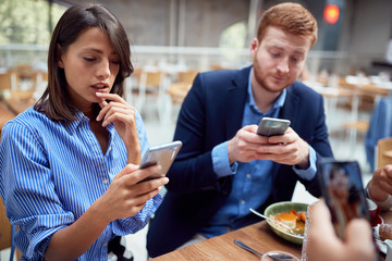 people at lunch distracted from each other by cell phones. not present, social issues, victims of modern technology