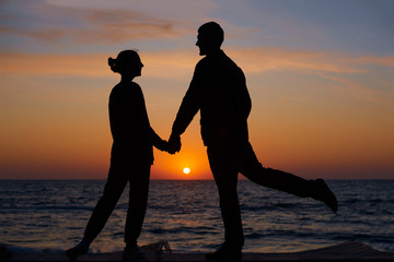 full body of a couple silhouette walking together on the beach at sunset