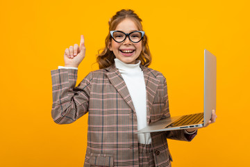 funny smart caucasian schoolgirl with glasses in a business suit and a jacket with a laptop in his...