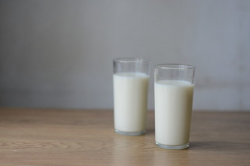 two glasses of milk on a wooden table on a gray background