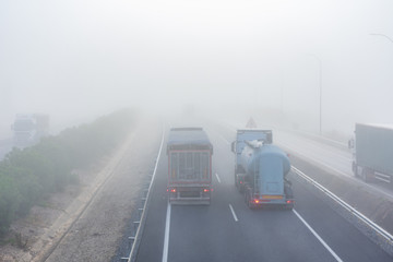 Several trucks driving in parallel on a highway with dense fog