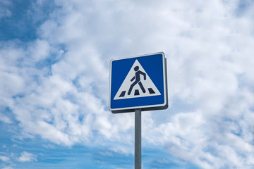 International traffic sign 'Pedestrian crossing'. Background contains cloudy blue sky