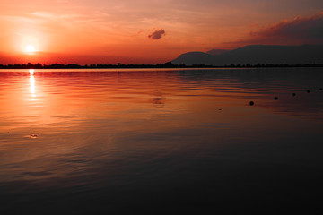 Cinematic red sunset sky reflected on the still waters of the Mekong River during the hot and humid summer season in Cambodia