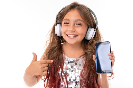 Little pretty caucasian girl listen to music with big earphones and recommed the phone, picture isolated on white background
