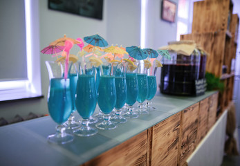 blue cocktails in tall glasses with lemon and paper umbrellas stand on the wooden bar counter