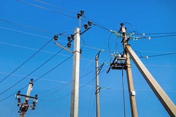 Multiple pillars of power line standing together close to each other. Clear blue sky is on background. View directed from bottom to up