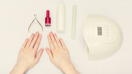 Manicure and nail Polish concept. Uv-lamp, nail clipper, woman's hands, closeup, white background, top view, 16:9