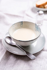 Cauliflower and Potato Cream Soup served with herbs and pepper on white linen striped tablecloth. Selective focus