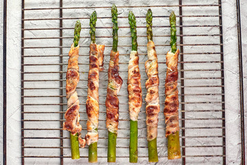 Fresh Organic Asparagus baked with bacon in the oven, close-up, top view