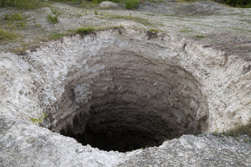 Black aperture of karst sinkhole, formed above abandoned limestone mine. Diameter about 15 ft,...