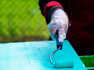 Woman's hand paints a sheet of plywood in turquoise color with a roller