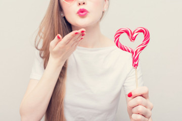 Woman sends air kiss with lollipop in the shape of a heart, cropped image, closeup, toned