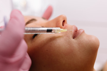 Injection in patient woman lips to volume and correction shape making by doctor cosmetologist. Beautician injects filler collagen or hyaluronic acid into lips with syringe. Contour Plastic of Lips.