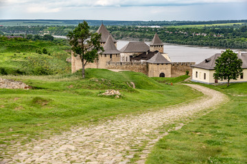 Fototapeta na wymiar Khotyn Fortress castle in Ukraine and the road to it, river on a background of dark clouds on a cloudy windy day in summer. Horizontal orientation.
