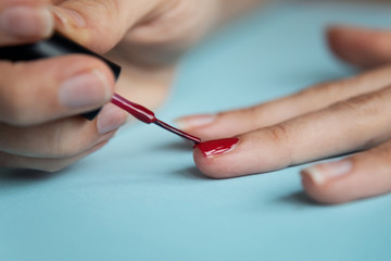 A woman painting her nails with red lacquer over blue background.