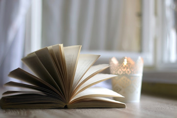 Lit candle in the candle holder and open book on a table. Selective focus.