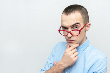 Nerd man with glasses thoughtfully looks at the camera and doubts something, portrait, white background, copy space