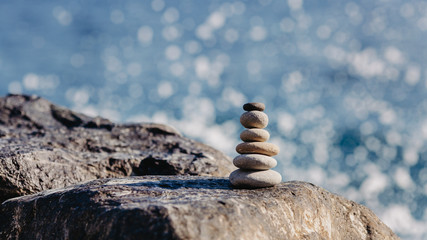 Stones pyramid on pebble beach, stability, zen, harmony, balance concept. With blur sea background on a sunny day.