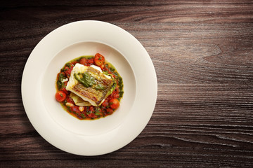 Plate of fish on vegetables served on wooden background