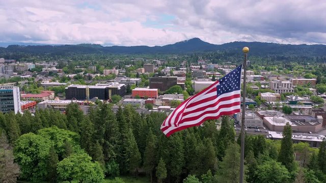 American Flag waving in aerial view of Eugene Oregon slowly flying around the flag.