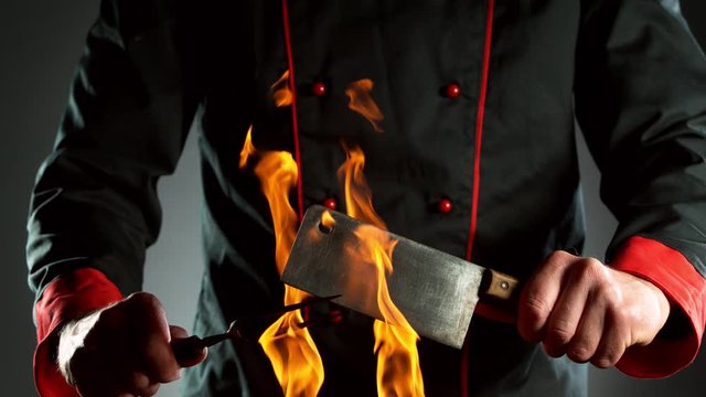 Super slow motion of closeup of chef with cleaver and fork above fire. Filmed on high speed cinema camera, 1000 fps.