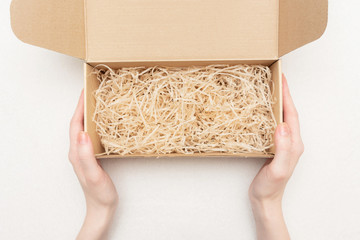 Woman shows an open gift box with decorative straw or shavings, women's hands, closeup, copy space, top view