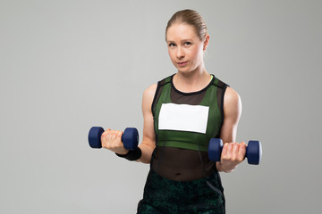 Fototapeta na wymiar strong blonde girl in sportswear holds dumbbells on a gray background