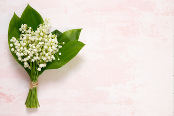Bouquet of flowers lily of the valley on pink table, top view, space for text, flat lay.