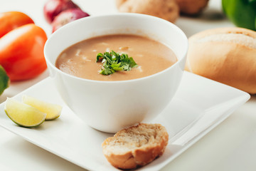 Bowl of creamy soup served with lemons and bread. Vegetables in the background.