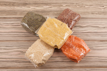 Cereals (lentils, red rice, mung bean, quinoa, millet) in transparent packages on a wooden background. Helping the needy