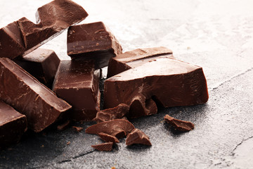 close up of bitter chocolate bars and broken piesces on rustic background.