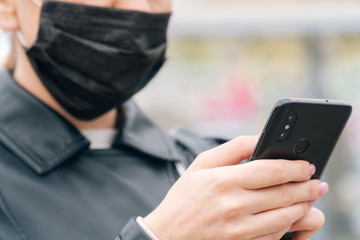 Close-up women's hands hold a phone against the background of a face in a medical mask. The concept of safety is about your health. Girl calls taxi