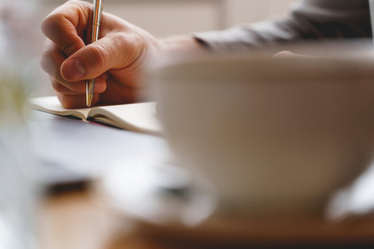 Young gentleman writing in notebook in cafe