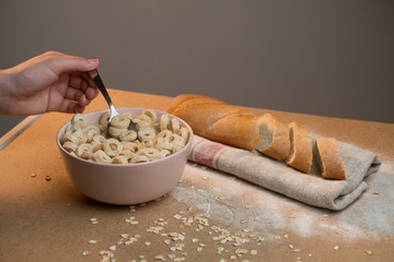 Close-up hand stirs flakes rings in a plate of milk. The concept of cooking breakfast with vegetable milk
