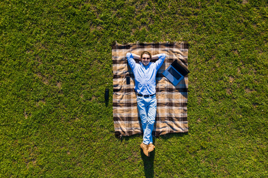 Happy Young Man With Laptop Relaxing On The Grass, View From Above