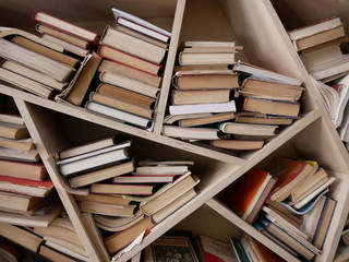 Fototapeta premium A self-made wooden bookshelf of unusual shape completely filled with new and old books of different thickness and sizes.
