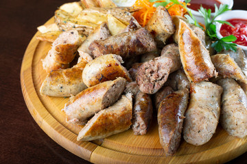 Homemade grilled sausages with sauerkraut and ketchup on a round wooden tray.