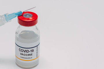 conceptual vial of covid-19 or coronavirus vaccine against a white background with a syringe leaning on the vial